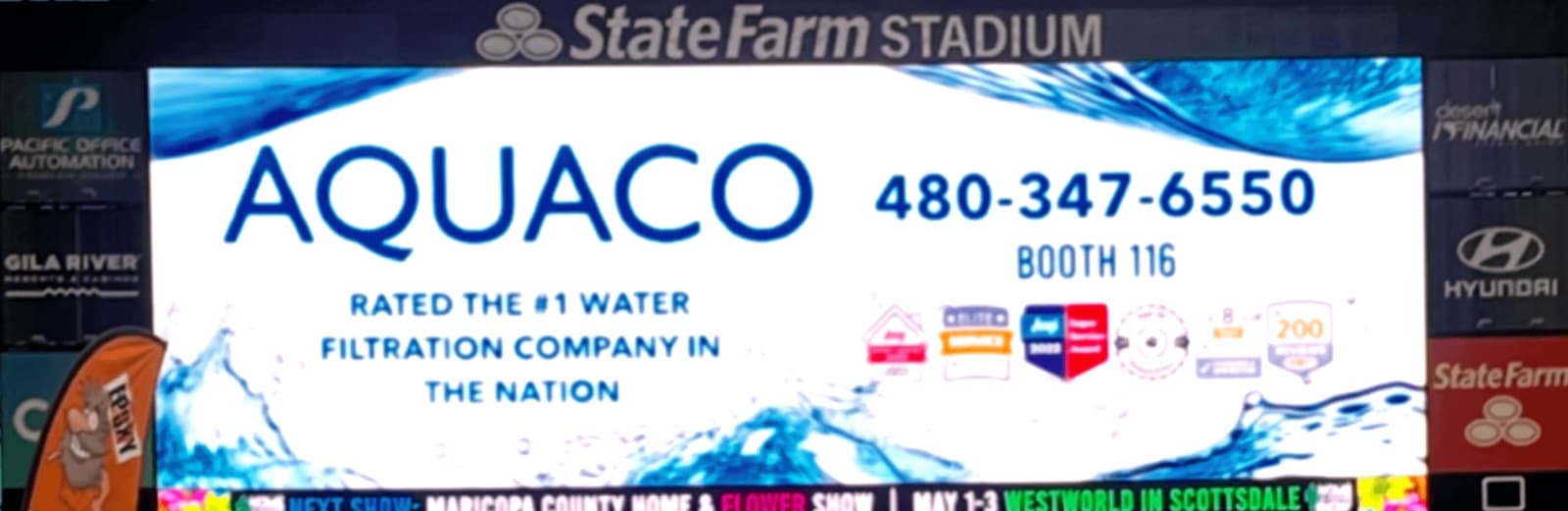An Aquaco advertisement on the video board at State Farm Stadium, carrying the company name, phone number, booth number and the wording “rated the #1 water filtration company in the nation”